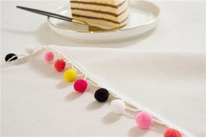 Close-up of the textured off-white tablecloth featuring colorful pom-pom edge detailing