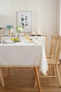 Detail of white cotton linen tablecloth featuring decorative tassels on a wooden table