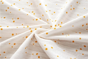Detail of yellow daisy embroidery and orange polka dots on white cotton fabric cloth