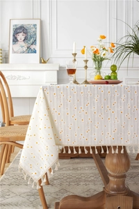 Detail of cotton tablecloth with orange daisy patterns and elegant beige tassel edges