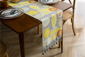 Detail of grey table runner with citrus fruit patterns and blue beaded tassel decoration