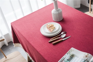 Detail of red linen-textured tablecloth with elegant white tassels on a wooden dining table