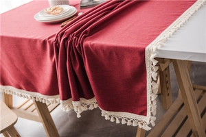 Close-up of red textured tablecloth with decorative beige tassel fringe on a modern table