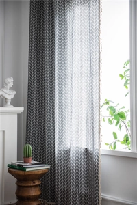Detail of grey geometric pattern curtain with beige tassel trim in a bright room