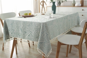 Detalle de mantel jacquard geométrico verde azulado con elegantes flecos de borlas blancas