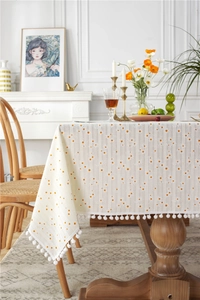 Detail of cream cotton tablecloth with orange daisies and white pom-pom fringe edges