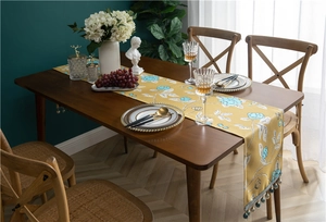 Close-up of ginger yellow table runner with blue floral patterns and tassel fringe detail