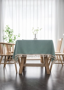 Close-up of sage green textured tablecloth with white cotton tassel ball fringe details