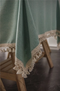 Close-up of sage green textured tablecloth featuring elegant cream tassels on corners