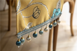 Detail of golden table runner with blue floral embroidery and fringe tassel trim