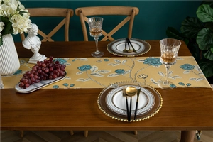 Detailed close-up of yellow table runner with blue floral patterns on a dark wooden table
