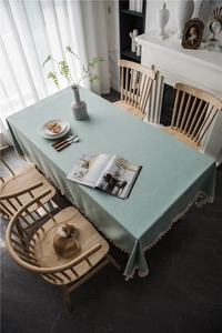 Detail of mint green rectangle tablecloth with tassels on a wooden dining table