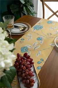 Detail of yellow polyester table runner with blue rose patterns and elegant fringe tassels