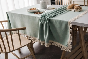 Detailed view of light green tablecloth with elegant beige fringe and woven texture