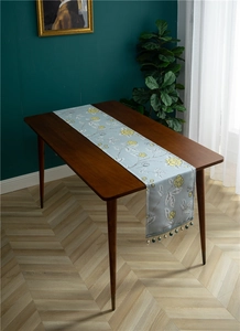 Close-up of floral embroidery and blue-gold beaded tassel on a polyester table runner