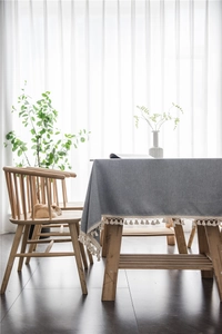Detailed view of grey blue tablecloth with white tassel fringe on wooden table