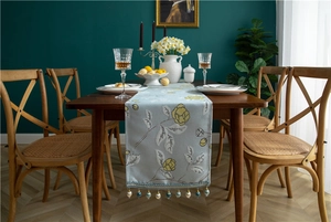 Detailed close-up of light blue table runner with yellow floral embroidery and bead tassels