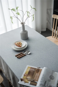Close-up of light grey tablecloth showing woven texture and cream tassel edge detail