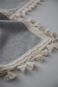 Macro detail of gray linen tablecloth texture with cream white bohemian fringe tassels