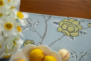 Detail view of light blue jacquard table runner with yellow floral patterns and tassels