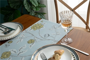 Detail of light blue table runner featuring yellow floral embroidery on a wooden table