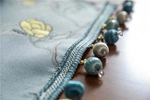Macro detail of polyester table runner featuring blue floral embroidery and fringe tassels