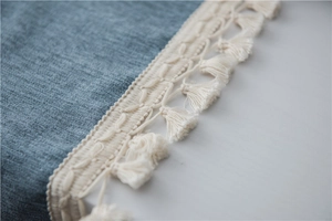 Close-up of textured blue tablecloth fabric with elegant off-white woven tassel fringe