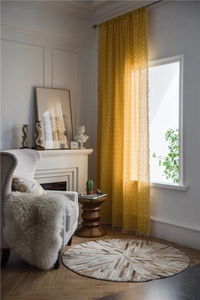 Detail view of yellow geometric print curtains with white tassels in a cozy living room