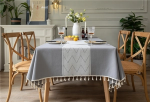 Macro detail of grey tablecloth featuring white geometric patterns and tassel edges
