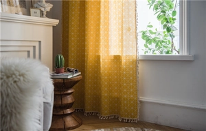 Close-up of yellow geometric grid curtain featuring delicate cream tassel fringe trim