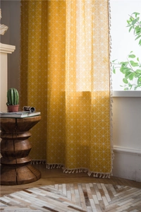 Detail of yellow cotton-linen curtain featuring white geometric grid and cotton tassels