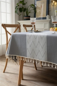 Close-up of grey jacquard tablecloth featuring white wave pattern and cream fringe tassels