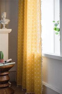 Detail of yellow geometric lattice curtain fabric with white tassels in soft natural light
