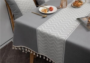 Detail of dark grey jacquard tablecloth with white wavy patterns and boho fringe edges