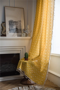 Close-up of yellow geometric plaid curtain with white tassels in a cozy home setting