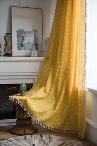Detail of yellow geometric grid curtain with white woven fringe tassels in home setting