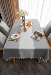 Detail of grey jacquard tablecloth featuring white wavy patterns and elegant fringe tassels