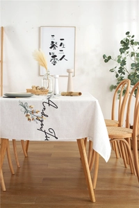 Detail of floral embroidery and cursive lettering on beige linen rectangular tablecloth