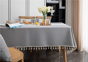 Close-up of grey jacquard tablecloth featuring detailed white wavy tassel edge and thick fabric