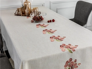 Detail of floral embroidery on a beige linen rectangular tablecloth in a cozy home setting