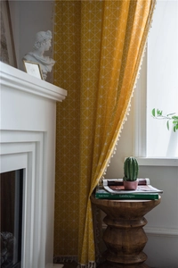 Detail of yellow geometric curtain with white fringe tassels in a cozy home setting