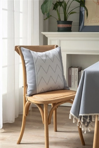 Detail of grey jacquard tablecloth with wave tassels and matching chevron cushion cover