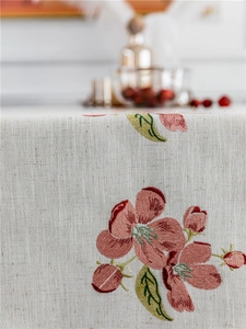 Close-up of pink flower embroidery on beige linen tablecloth with fine stitching details