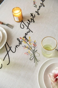 Detailed close-up of floral embroidery and cursive lettering on beige linen tablecloth