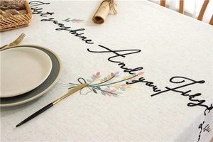 Close-up of embroidered floral patterns and script lettering on beige linen tablecloth