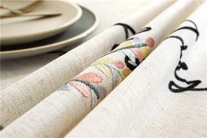 Detail of leaf embroidery and 'Happy' text on beige linen tablecloth fabric