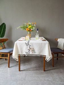 Detailed close-up of embroidered floral patterns and black script on white fringed tablecloth