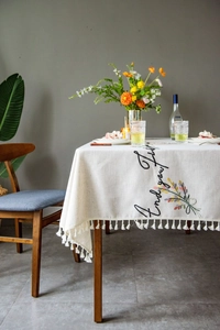 Detail of white linen tablecloth with 'Enjoy life' embroidery and delicate fringe edges