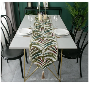 Detail of tropical leaf pattern table runner with soft brown tassels in a modern dining setting