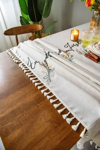 Close-up of floral embroidery and cotton tassels on a beige linen tablecloth